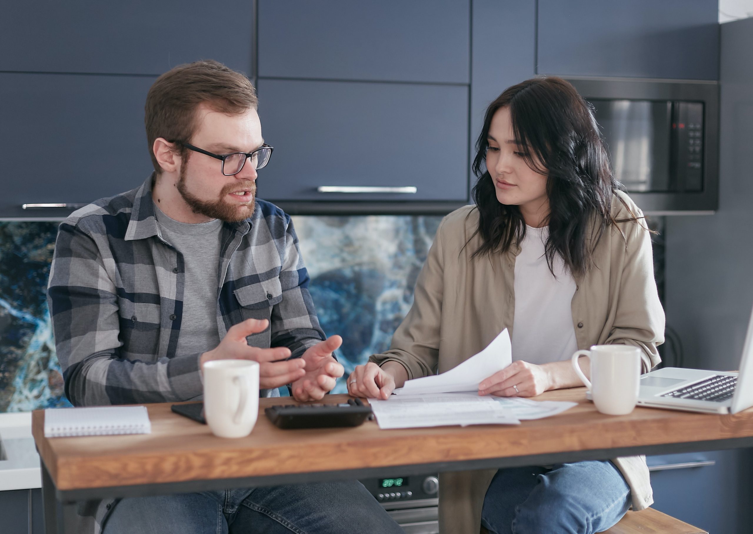 Couple talking in a serious but calm manner over a table full of paper and mugs. Healthy relationships have problems