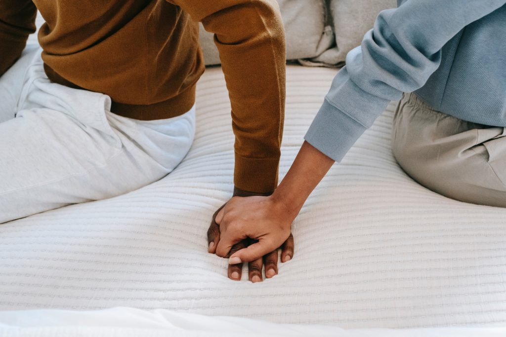 Couple holding hands while sitting in bed. Why sex is good for you