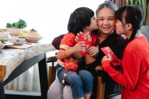 Kids kissing a female caregiver with red cards on their hands for Lunar New Year.