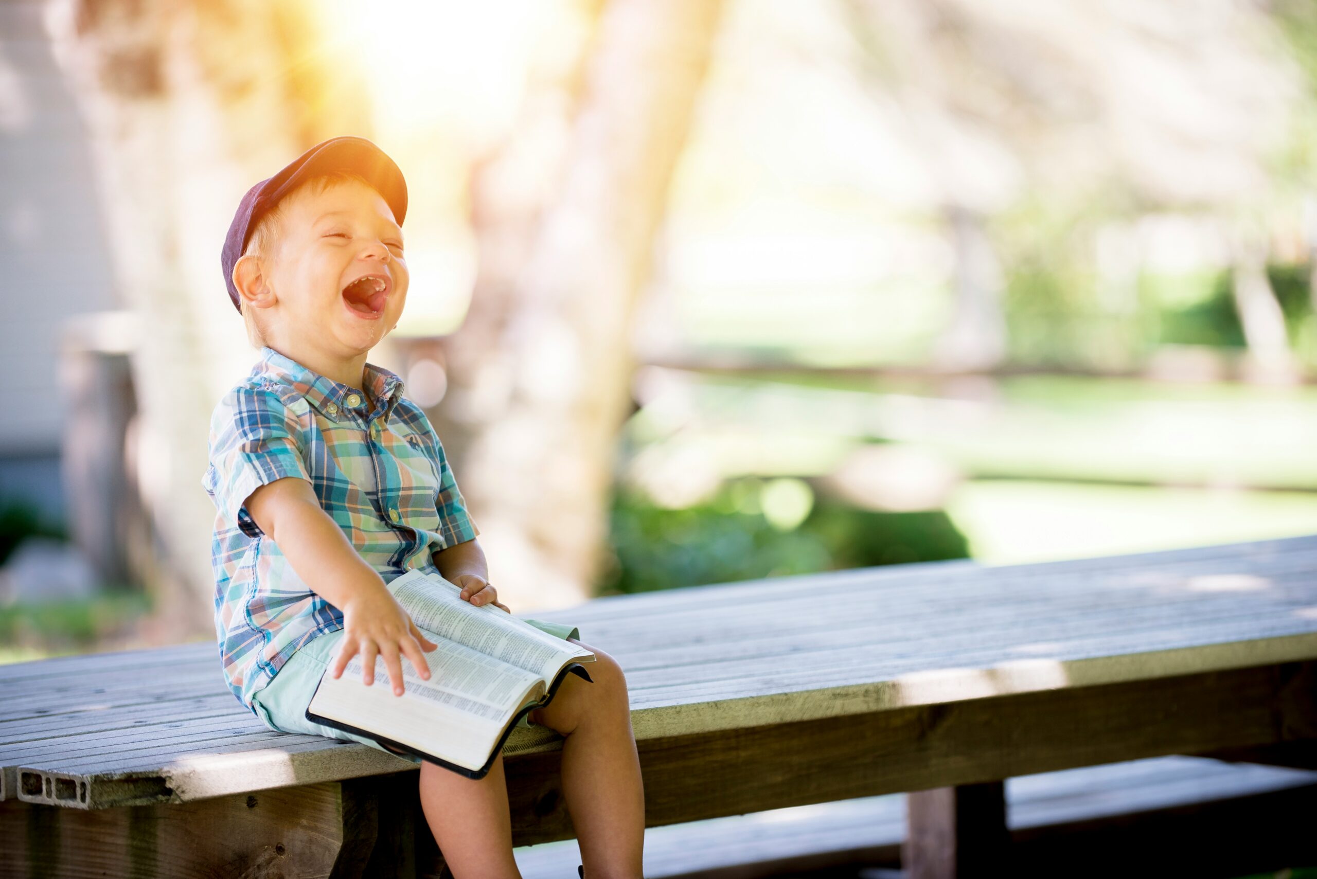 toddler boy sitting on a bench holding an open book laughing happily. transforming past hurts into secure connections