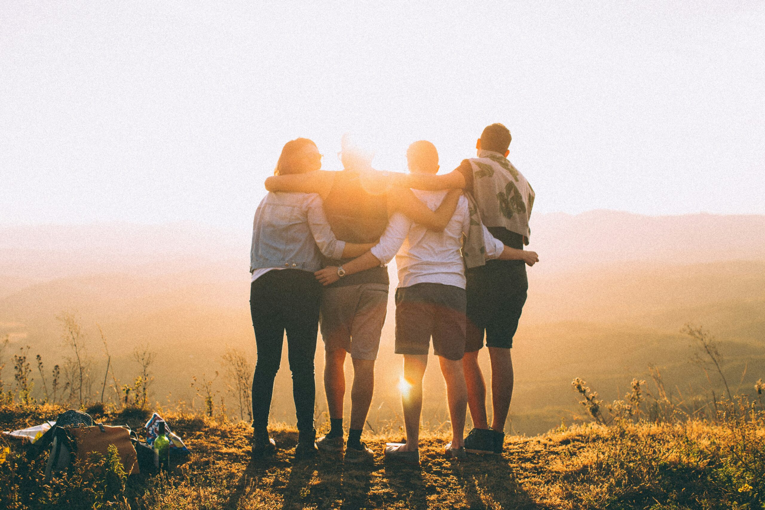 group of four friends with arms draped across each other's shoulders and with their backs toward the audience looking out into the horizon on top of a cliff. starting with what matters most