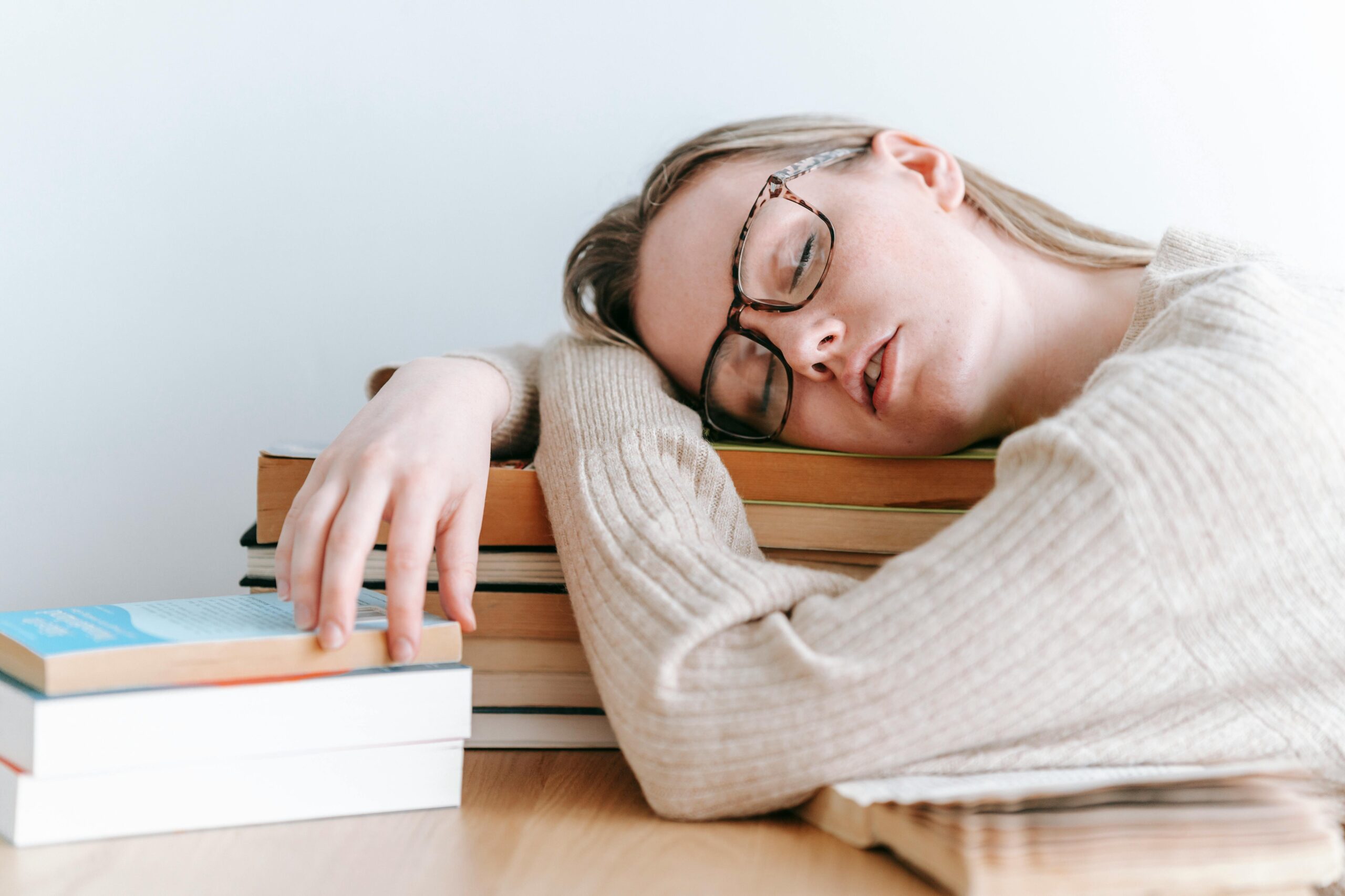 sleeping girl lying on top of a stack of books on her desk. The Silent Relationship Killer.