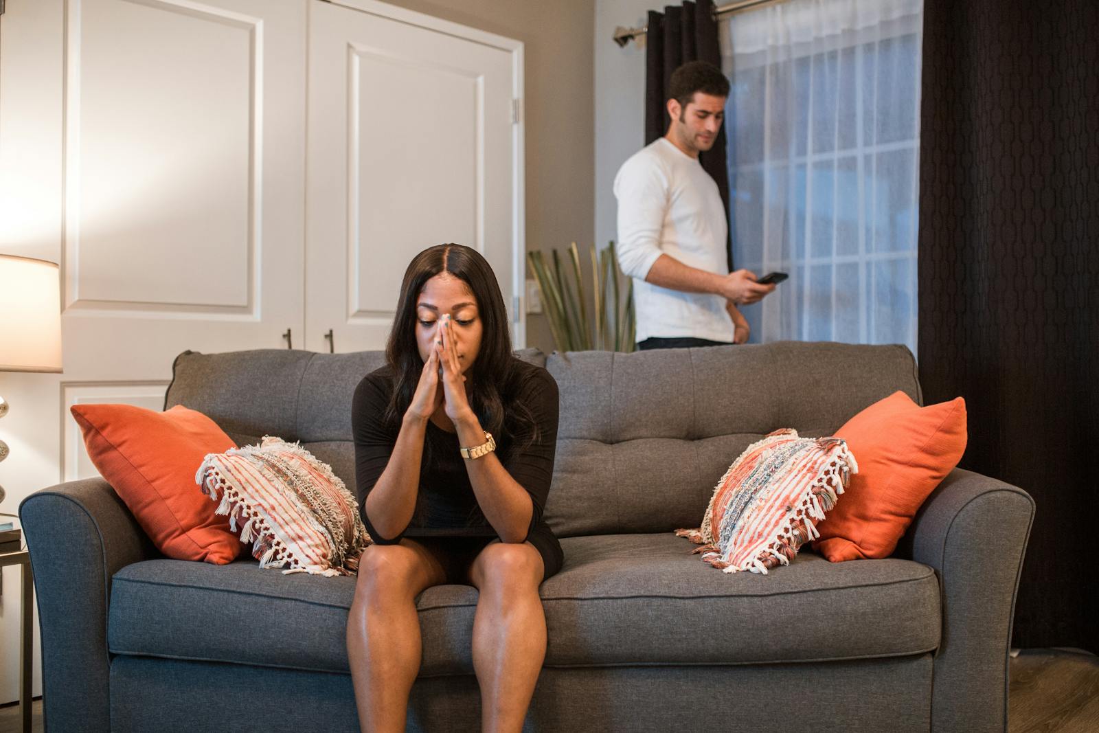 woman sitting on sofa while man stands apart hoping relationship magically changes